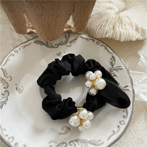 Detailed close-up of a black silk scrunchie with faux pearls on an elegant ceramic plate