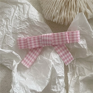 Close-up of pink and white plaid fabric bow hair clip on artistic white paper background