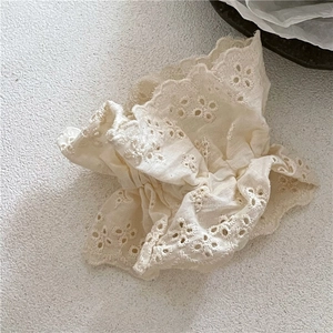 Detail eines cremefarbenen Spitzen-Scrunchies mit Stickerei und weicher Baumwollstruktur