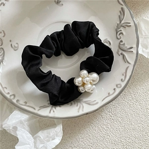 Detail of a black satin scrunchie with a cluster of white faux pearls on a ceramic plate