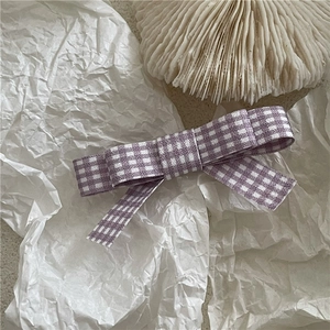 Detailed view of a purple plaid bow hair clip with ribbons on white textured paper