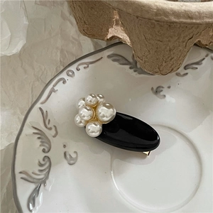Elegant black oval hair clip with white pearls on a decorative white porcelain saucer