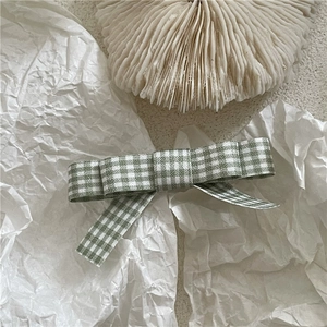 Detailed close-up of green and white plaid fabric bow hair clip with fine textile texture