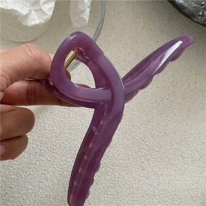 Close-up of a purple jelly-textured hair claw clip with cross design and metal spring