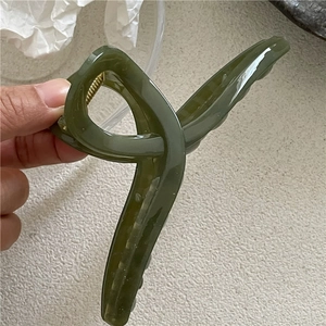 Detail of olive green cross-design hair claw clip with glossy jelly texture and metal spring