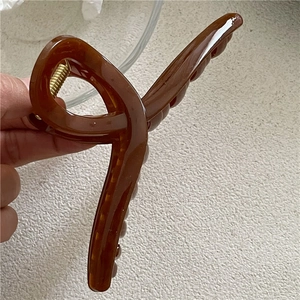 Detailed close-up of a large brown jelly hair claw clip with golden metal spring