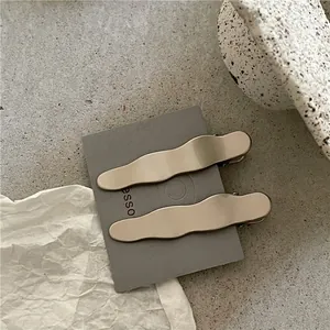 Vue détaillée de barrettes à cheveux dorées mates ondulées sur une carte grise minimaliste