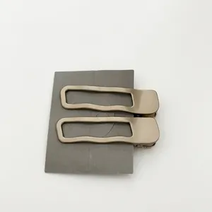 Barrettes à cheveux géométriques dorées mates avec design ondulé sur carte grise