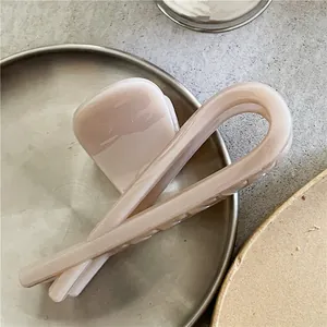 Vue détaillée de la pince à cheveux croisée en résine beige sur un plateau en métal