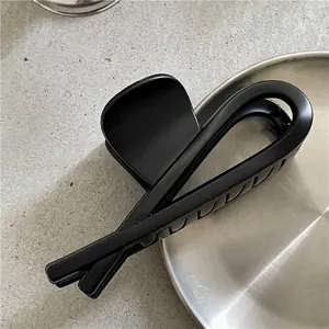 Détail de la pince à cheveux noire mate avec design géométrique croisé sur plateau
