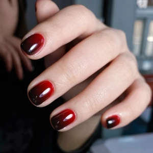 Close-up of short square-oval press-on nails with shiny red and black ombré gradient