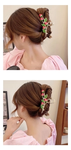 Detail view of large gold claw clip with red strawberry motifs on a woman's hair bun