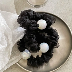 Elegant black tulle scrunchie with iridescent pearls on a minimalist metallic plate