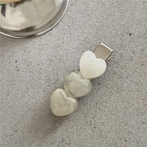 Detail view of cream marble heart hair clips on a textured stone surface backdrop