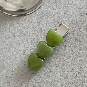 Detail showing three green heart-shaped resin charms on a silver metal duckbill hair clip