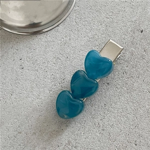 Close-up of three blue marble heart hair clips on a textured stone background