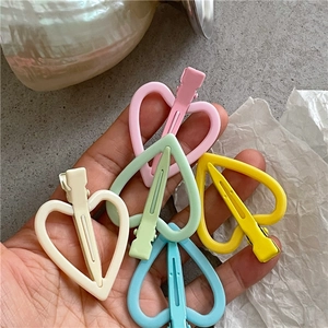 Cinq barrettes à cheveux en forme de cœur aux tons pastel macaron tenues en main