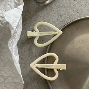 Détail de deux pinces à cheveux coeur crème au fini mat sur un fond texturé élégant