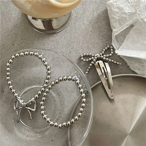 Polished silver beaded bracelet and bow hair clip set on a stylish textured background
