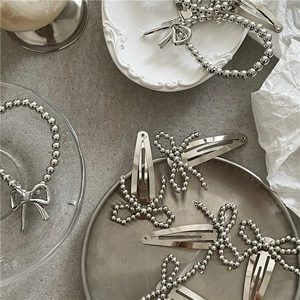 Silver beaded bow hair clips and metallic beaded hair ties on a white ceramic plate