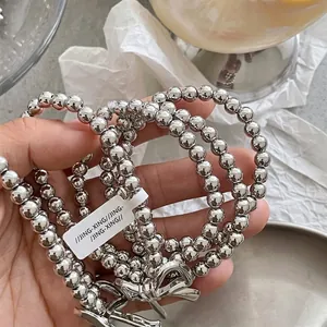 Silver beaded hair tie with a polished alloy bow pendant held in hand for a stylish look