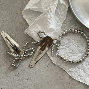 Detailed view of silver beaded hair clips and bow bracelet on minimalist art paper