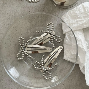 Close-up of three silver beaded bow hair clips on a textured gray background