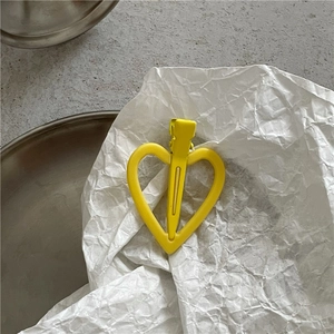 Vue détaillée d'une pince à cheveux jaune en forme de cœur sur un fond minimaliste chic