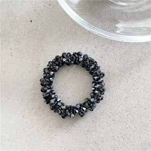 Dettaglio dell'elastico per capelli con perle di cristallo nero sfaccettate su fondo grigio