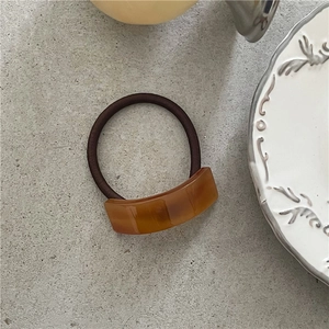 Detail of amber-toned tortoiseshell acetate hair tie on a minimalist grey stone surface