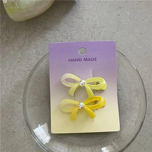 Détail de deux barrettes nœuds en dégradé jaune avec strass sur leur emballage