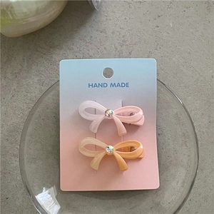 Détail de deux pinces à cheveux nœud en résine colorée avec cristal sur support
