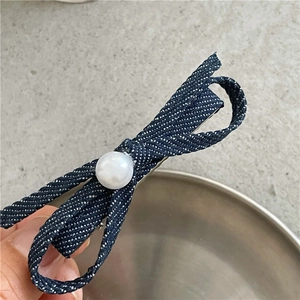 Detail view of denim bow hair clip with white polka dots and central faux pearl accent