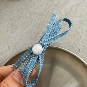 Close-up of denim bow hair clip with white pearl and natural frayed edges on metal clip