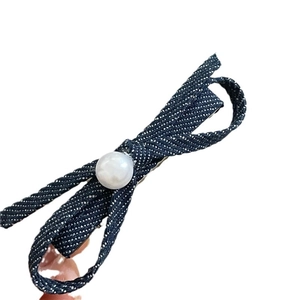 Denim bow hair clip with central faux pearl and white dotted texture on white background