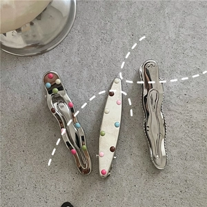 Dettaglio di tre fermagli per capelli a pois colorati e argento su superficie in pietra