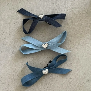 Trois barrettes en denim bleu avec détails cœur argenté sur un fond en pierre grise