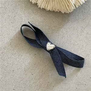 Détail d'une pince à cheveux nœud en denim à pois blancs et breloque cœur argentée