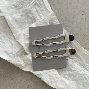 Vue détaillée de pinces à cheveux ondulées en métal argenté sur un carton gris texturé