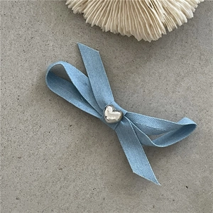 Détail de la pince à cheveux nœud en denim bleu clair avec un cœur métallique argenté