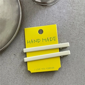 Vue détaillée de deux barrettes rectangulaires beiges mates sur carte jaune