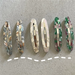 Detail view of six oval acetate hair clips with marble textures and metal spring clips