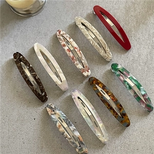Detail view of nine patterned acetate oval hair clips arranged on a textured grey background
