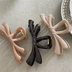 Three jelly texture bow hair claws in caramel, black and beige on stone surface