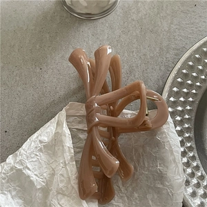 Macro detail of nude pink acrylic bow hair claw clip showing golden metal spring