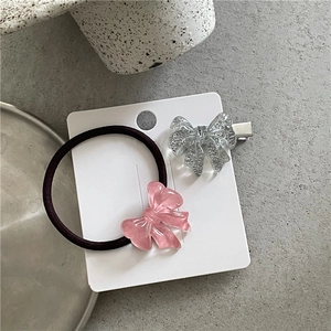 Close-up of pink glitter resin bow hair tie and clip set on a white display card