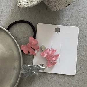 Detail view of pink resin bow hair clips and ponytail holder on a metal tray
