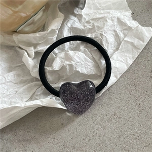 Detailansicht von schwarzem Haargummi mit glitzerndem lila Herzanhänger aus Kunstharz
