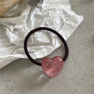 Detailaufnahme eines schwarzen elastischen Haargummis mit glitzerndem rosa Herzanhänger