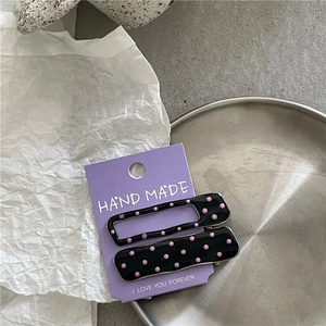 Close-up of black alloy hair clips with pink polka dots on a purple display card